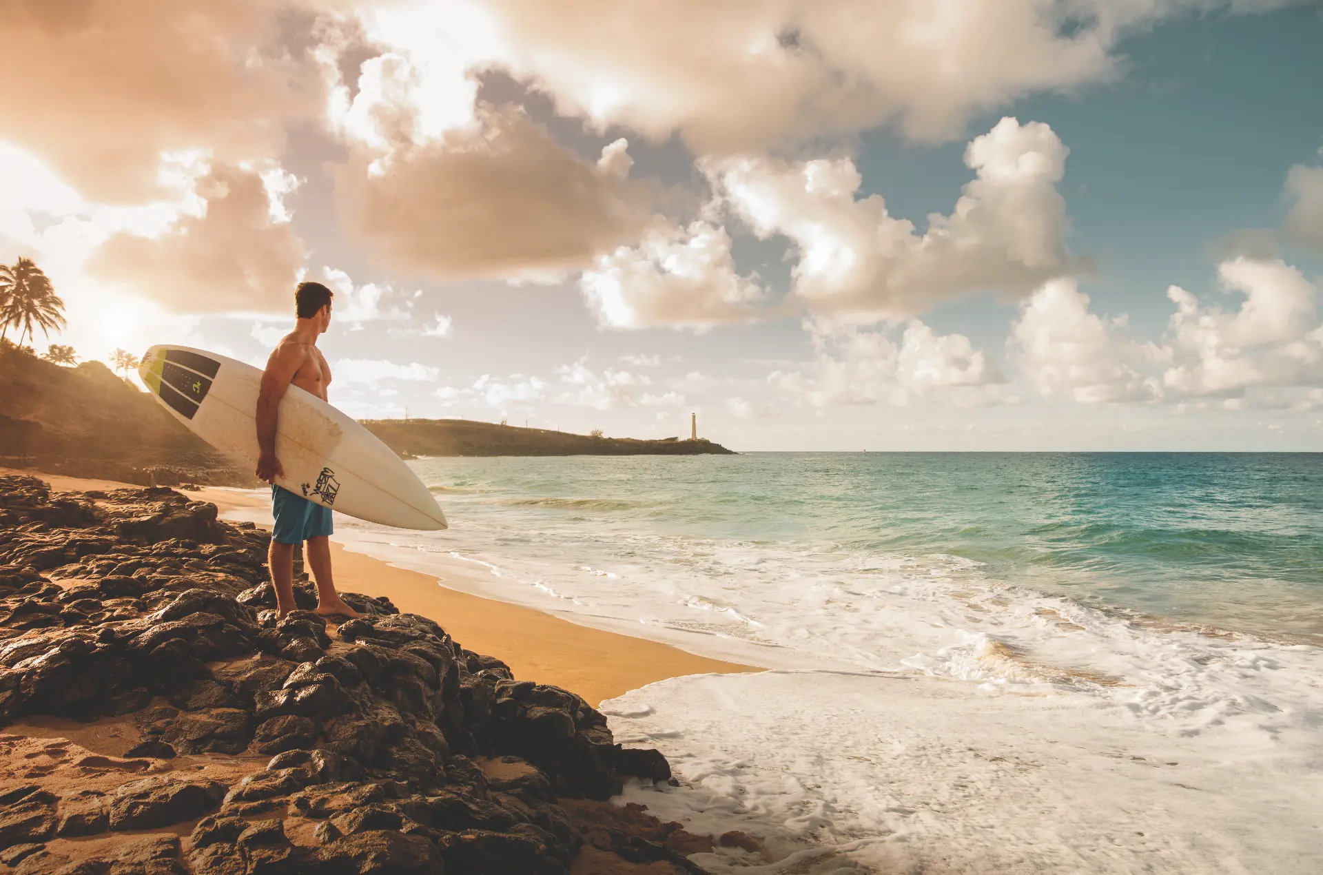 Surfer on the rocks at sunset on Kauaʻi